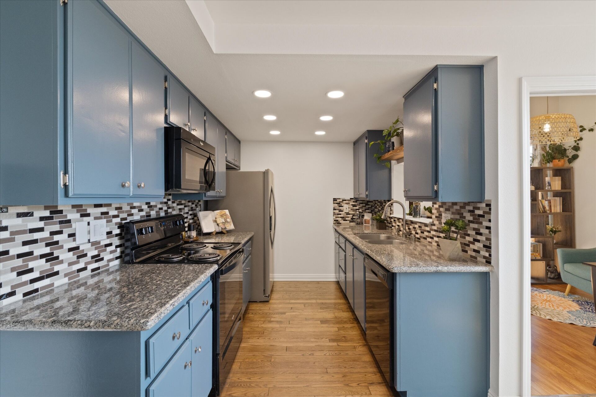 Galley kitchen with blue cabinetry, granite counters, and stainless appliances